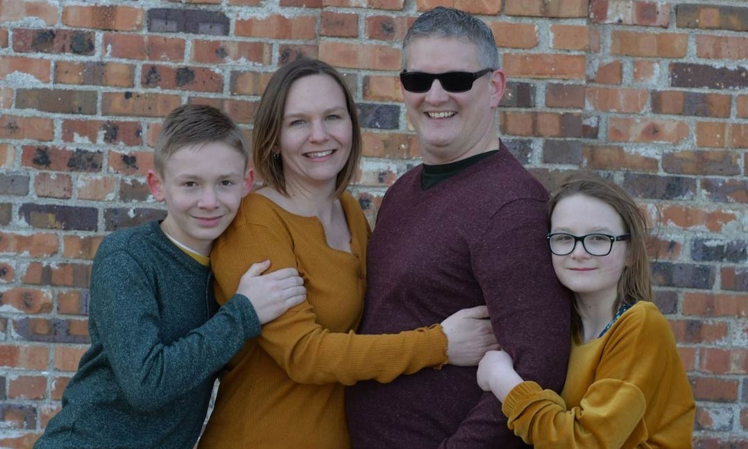 Man wearing glasses with his smiling wife, and happy son and daughter