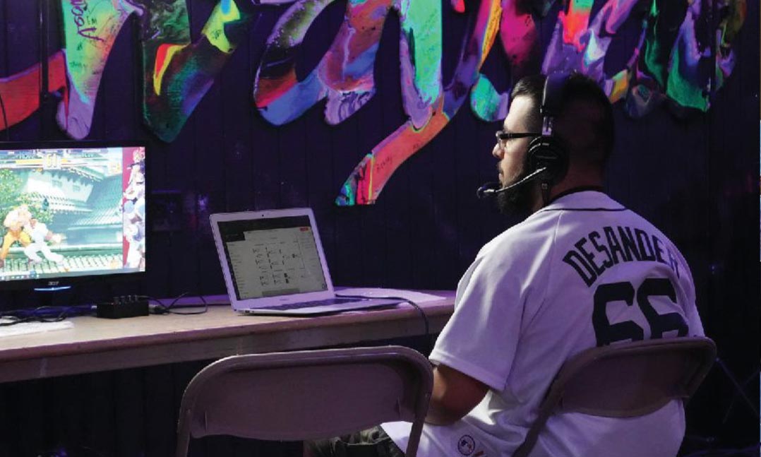 A video gamer sits at a desk in front of a computer and oversized monitor