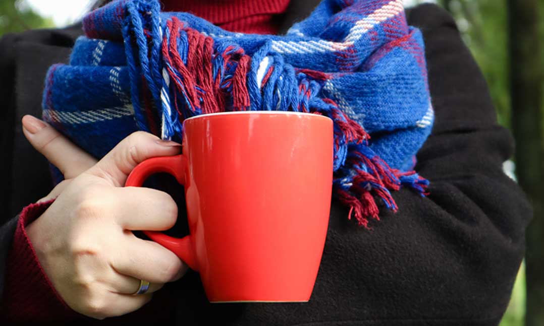 person wearing a scarf holding a mug